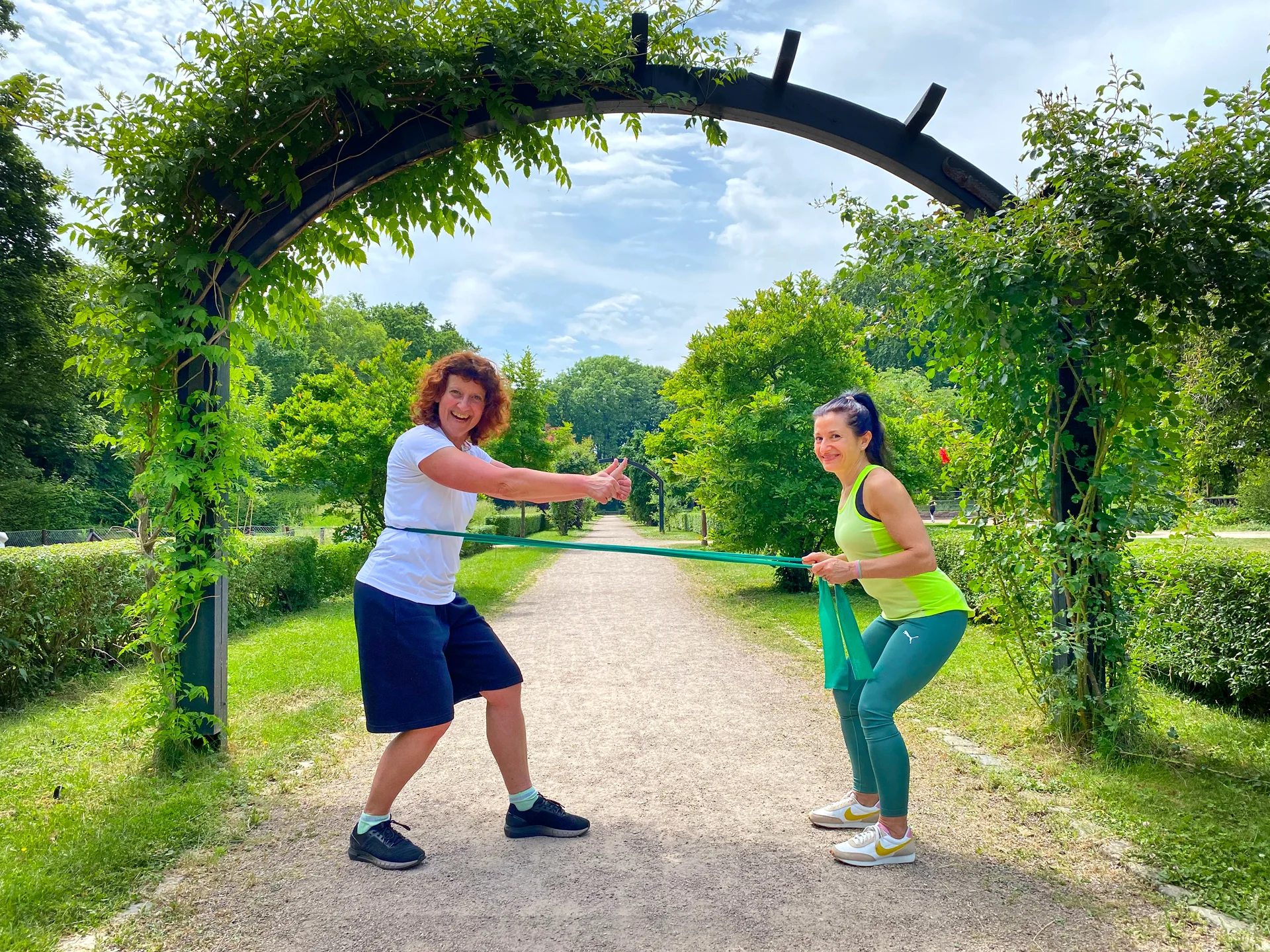 Funktionelles Outdoor-Training: Rudern mit dem Theraband unter Anleitung der Trainerin im Park.