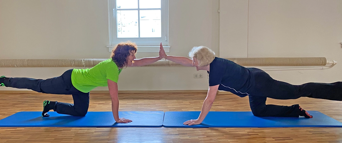Trainerin und Kundin führen Partnerübung im Kniestand aus – funktionelles Seniorentraining für Koordination und Rumpfstabilität