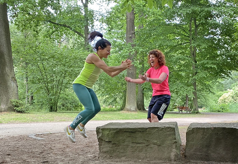 Funktionelles Training mit Sprungkraft: Kundin wird von Trainerin zum Sprung auf einen Steinblock angeleitet.