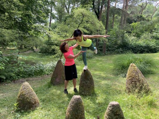 Personal Trainerin Marion Kinzig leitet Kundin bei einer Standwaage auf einem Stein im Grünen an – So geht Progression im funktionellen Training.